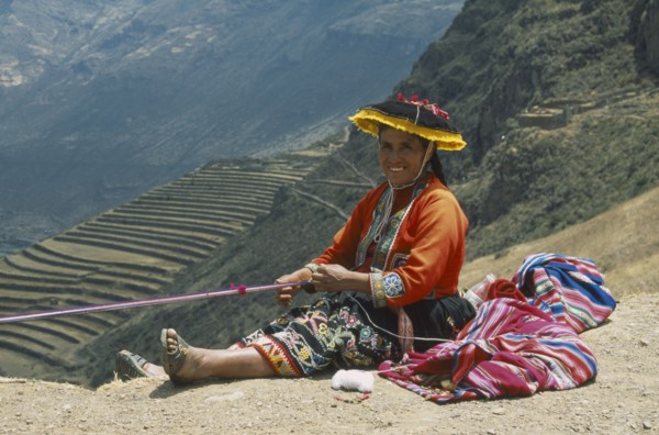 PERU, Cusco, Pisac, "Quechuan Indian woman weaving, inca terracing behind. Sacred Valley"