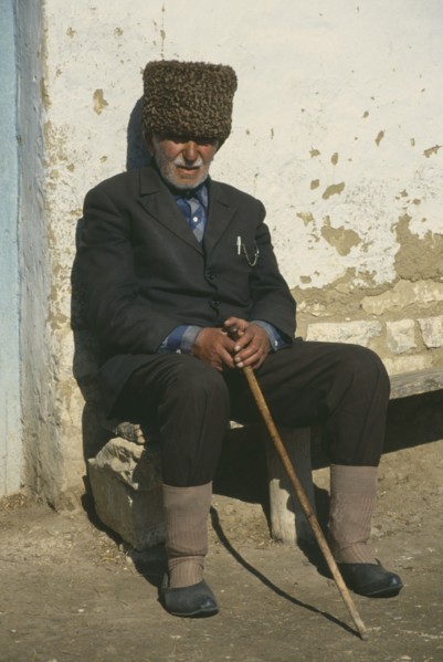 RUSSIA, Dagestan, Sadah, Elderly local man sitting outside wall of building.