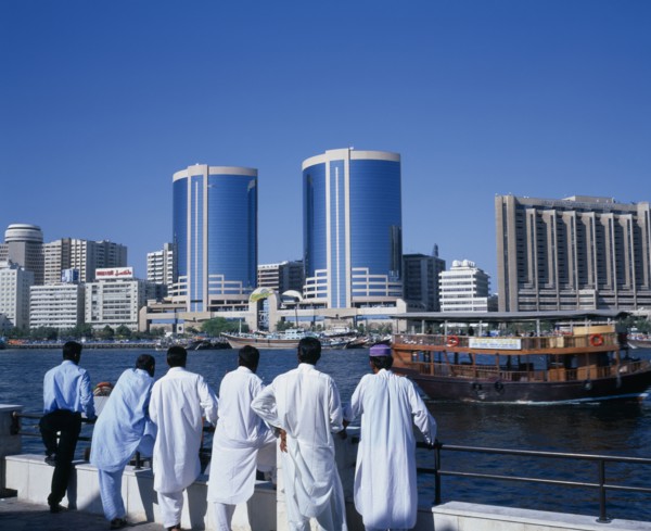 UAE, Dubai, Dubai Creek.  Men standing on waterfront looking out towards city skyline and passing