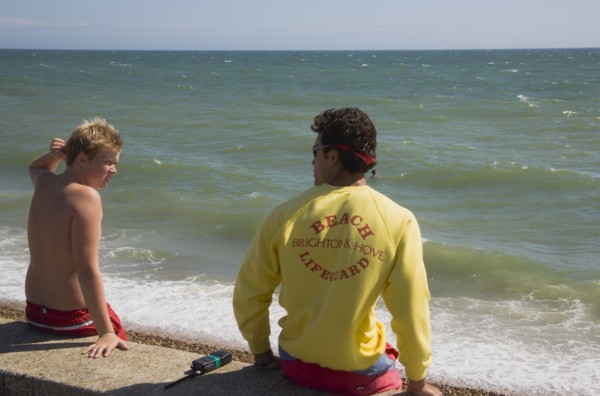 ENGLAND, East Sussex, Brighton, Life guard talking to young boy on the sea wall at Hove.