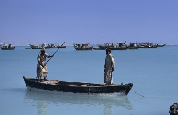 QATAR, Khor, Fishermen in a wooden canoe with fishing boats at anchor beyond