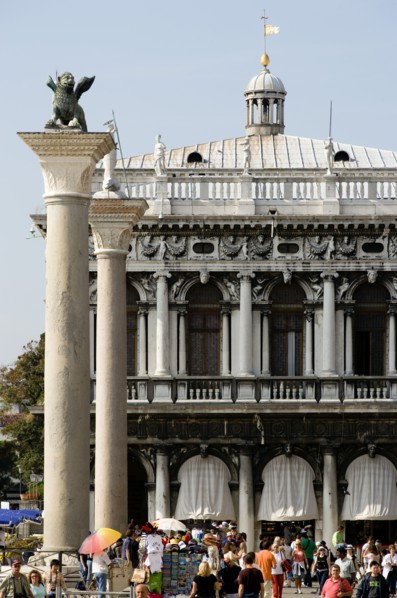 ITALY, Veneto, Venice, Tourists walk in the Piazetta below the winged Lion of Saint Mark on the