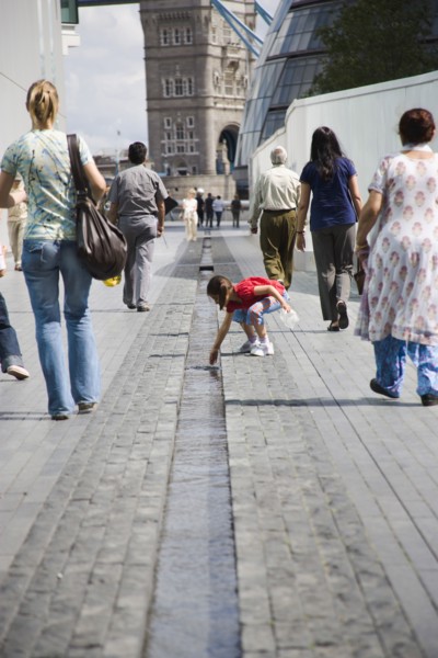 ENGLAND, London, People walking passed man made stream toward GLA town hall and Tower Bridge.
