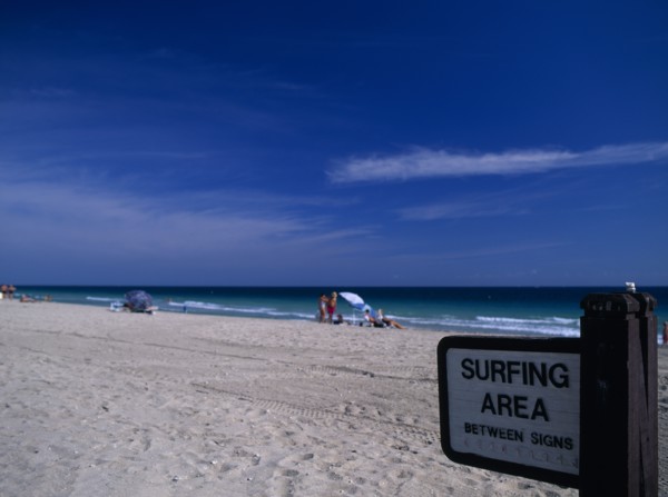 USA, Florida, Fort Lauderdale Beach, Designated Surfing Area Sign on sandy beach with sunbathers