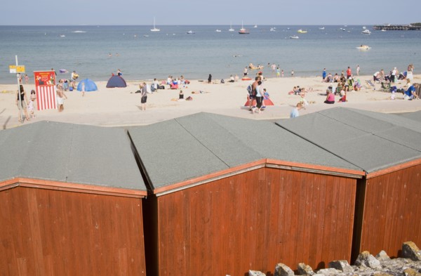 ENGLAND, Dorset, Swanage Bay, View across beach hut roofs towards busy sandy beach and sea