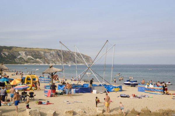 ENGLAND, Dorset, Swanage Bay, Busy colourful sandy beach scattered with inflatables and windbreaks