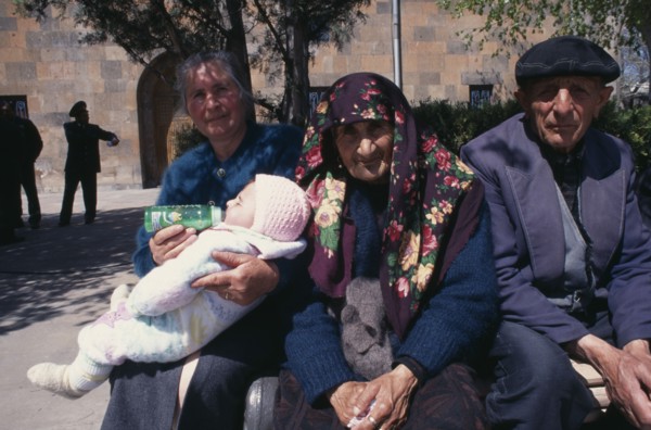 ARMENIA, Echmiadzin, Woman bottle feeding baby beside elderly couple sitting in sunshine.