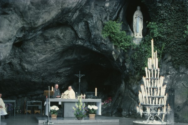 FRANCE, Midi-Pyrenees, Hautes-Pyrenees, Lourdes.  Priest conducting service at cave shrine in