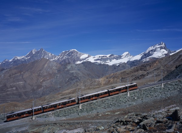 SWITZERLAND, Valais, Zermatt, "Gornegrat Railway with train traveling past snow capped mountains