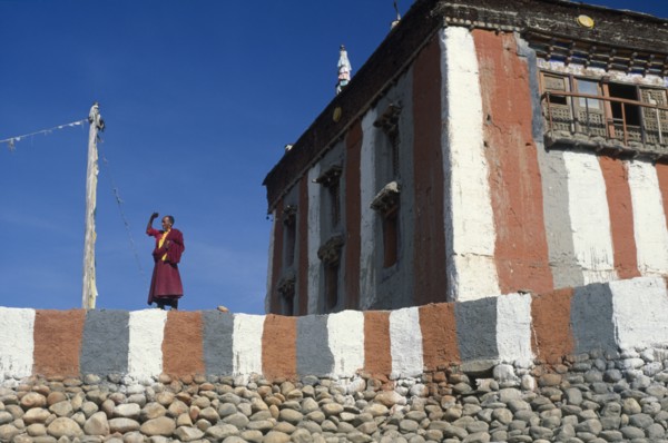 NEPAL, Mustang, Tsarang Gompa, "Tibetan Buddhist monk looking out from monastery terrace, shielding