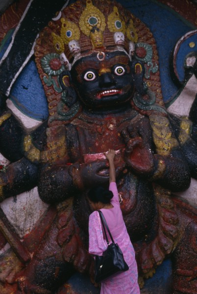 NEPAL, Kathmandu, Woman making offerings at the Kala Bhairab or black Shiva in Durbar Square