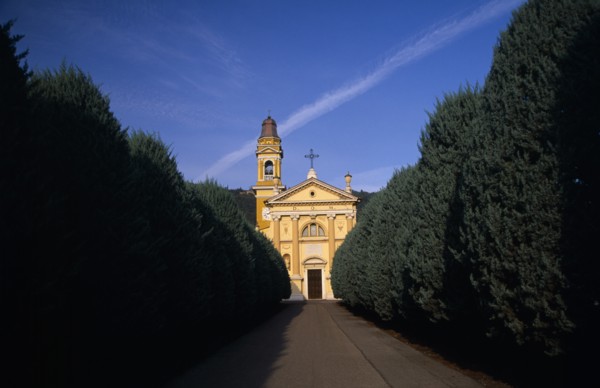 ITALY, Lombardy, Yellow and white exterior facade of small church with bell / clock tower at side