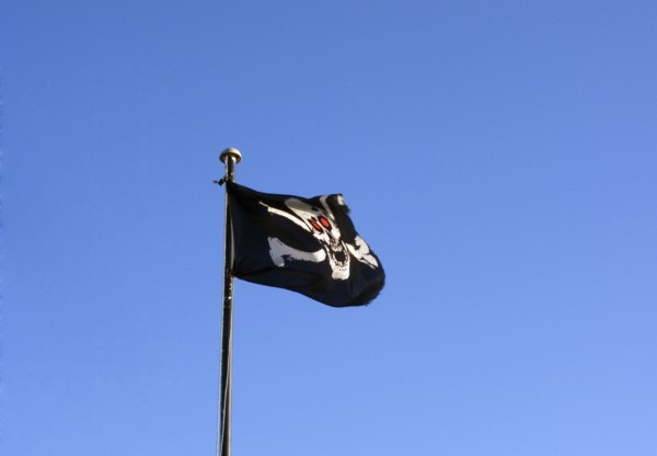 ENGLAND, East Sussex, Hastings, Skull and cross bones pirate flag flying against a blue sky