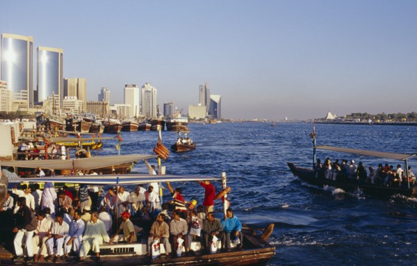 UAE, Dubai, Dubai Creek, Abra water taxis with passengers on Creek with city skyline beyond.