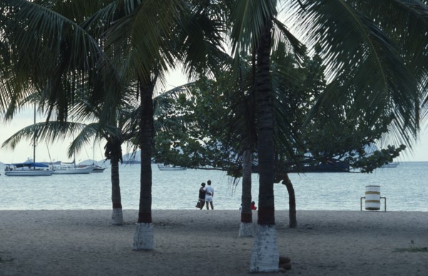 VENEZUELA, Estado Anzoategui, Puerto La Cruz, Couple on beach looking out over water and moored