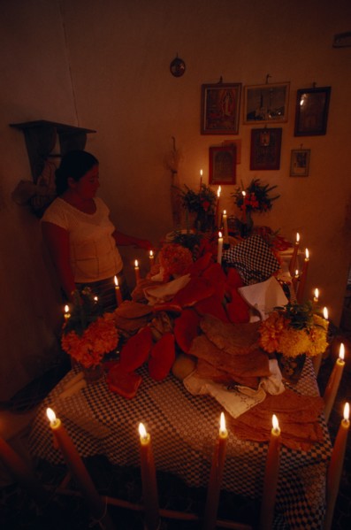 MEXICO, Acatlan, Woman lighting candles around altar for Day of the Dead covered with food and