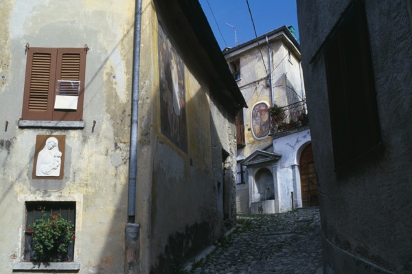 ITALY, Lombardy, Arcumeggia, Narrow cobbled street with fresco decoration and plaster relief of the