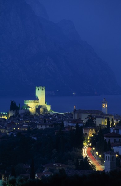ITALY, Veneto, Lake Garda , Malcesine.  Tiled rooftops of town and castle illuminated at night with