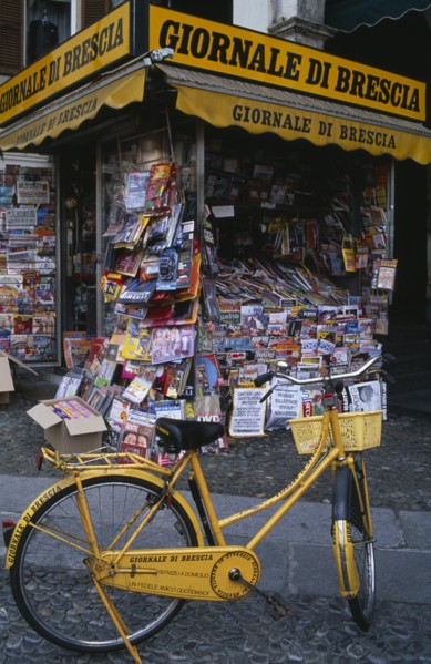 ITALY, Lombardy, Brescia, Piazza della Loggia.  Newspaper stand with yellow painted bicycle
