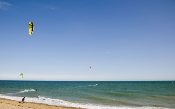ENGLAND, West Sussex, Lancing, Kite Surfers on sea next to shingle beach in the summer with blue