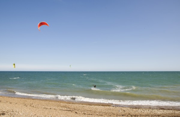 ENGLAND, West Sussex, Lancing, Kite Surfers on sea next to shingle beach in the summer with blue