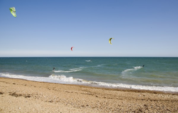 ENGLAND, West Sussex, Lancing, Kite Surfers on sea next to shingle beach in the summer with blue