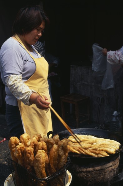 CHINA, Shanghai, "Woman using long pair of chopsticks to turn frying food in large, shallow dish in