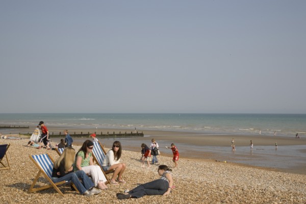 ENGLAND, West Sussex, Bognor Regis, A group of girls sitting on deck chairs on shingle beach with