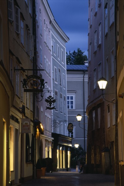 AUSTRIA, Salzburg, "Narrow street of Judengasse at night lined by tall, grey, pink and cream
