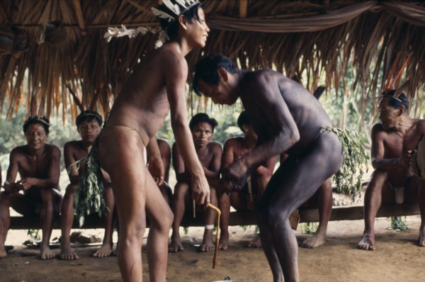 COLOMBIA, North West Amazon, Vaupes, Pair of Maku men taking part in dance watched by others seated