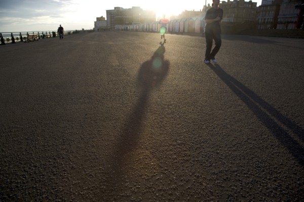 ENGLAND, East Sussex, Brighton, Silhoetted joggers on the seafront at Hove Lawns.