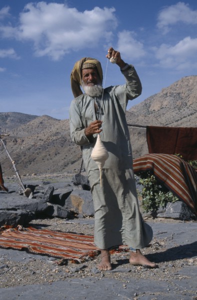 UAE, Oman, Jabal Shams, Elderly man using spindle to spin thread for rug making.