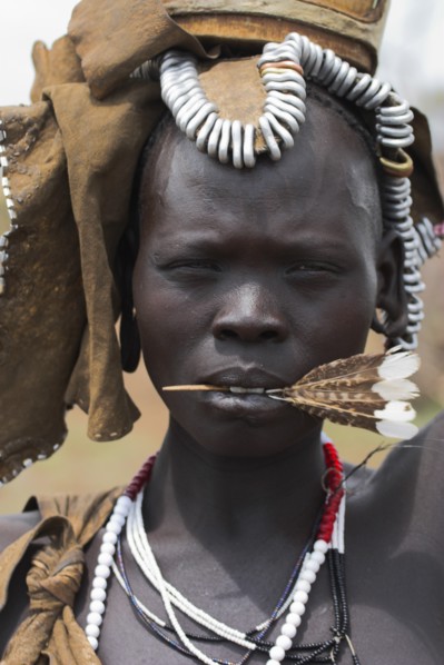 ETHIOPIA, South Omo Valley, Mursi Tribe, Portrait of woman with feather in her mouth.