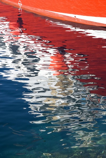 SPAIN, Canary  Islands, Lanzarote, Reflection of red hull of boat in rippled waters of the harbour