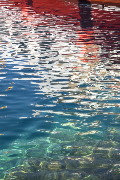 SPAIN, Canary  Islands, Lanzarote, Red and white reflection of boat in rippled water of harbour