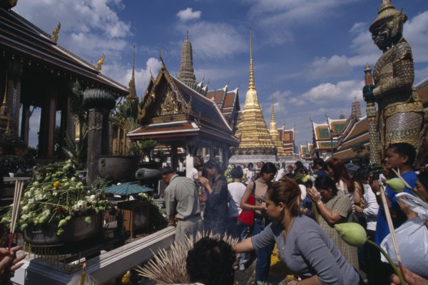 THAILAND, Bangkok, Crowds making offerings of incense and lotus flower buds at shrine in the Royal