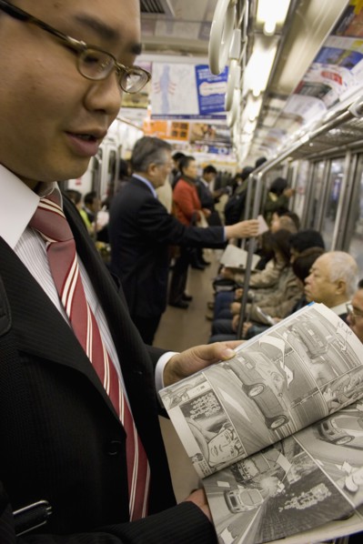 JAPAN, Honshu, Tokyo, Young Japanese man wearing a suit showing the Manga comic he is reading to