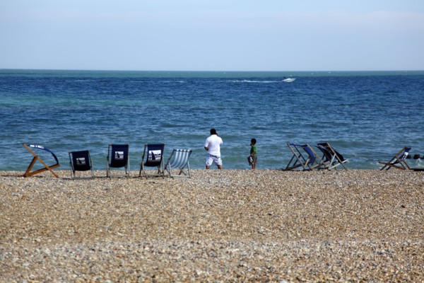 ENGLAND, East Sussex, Eastbourne, Man and young boy on the beach with deck chairs blowing in the