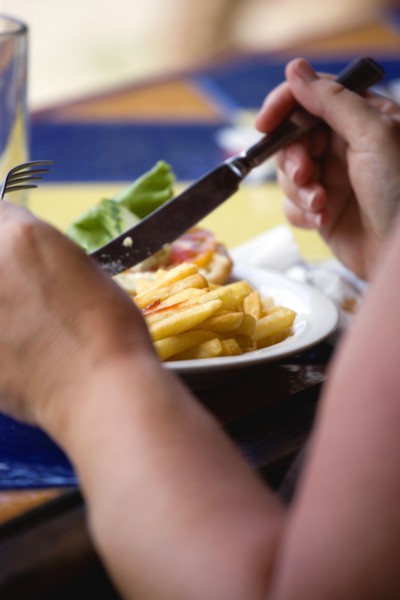 WEST INDIES, Grenada, St George, Sunburnt white caucasian woman eating a plate of potato chips and