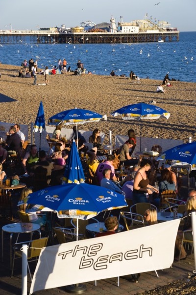ENGLAND, East Sussex, Brighton, People sitting under sun shade umbrellas at tables on the promenade