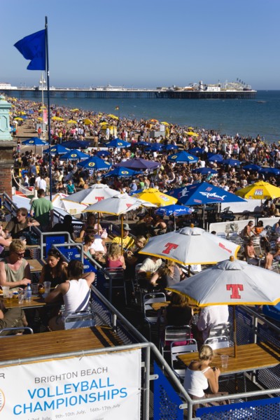 ENGLAND, East Sussex, Brighton, People sitting under sun shade umbrellas at tables on the promenade