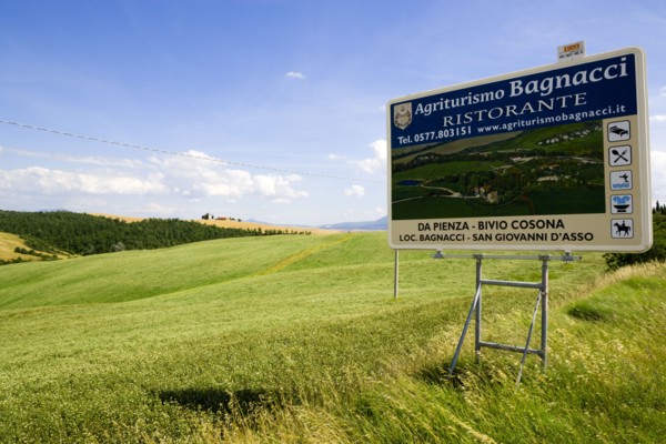 ITALY, Tuscany, Val D'Orcia, Agritourism sign for restaurant in field of ripe crops in the valley