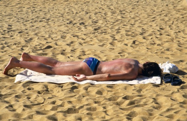 Sri Lanka, Negombo, Single man sunbathing on towel on sand of beach and turning red with sunburn.