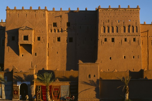 MOROCCO, Ouarzazate, View of red stone kasbah exterior with carpets hanging from the lower walls.