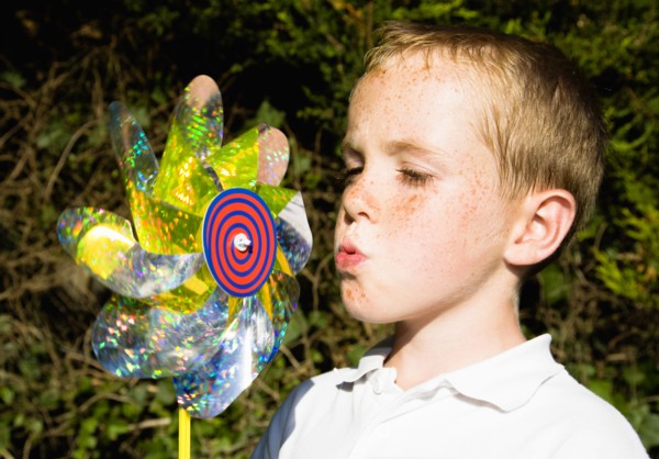 Children, Toys, Outdoors, Young boy blowing toy windmill gently.