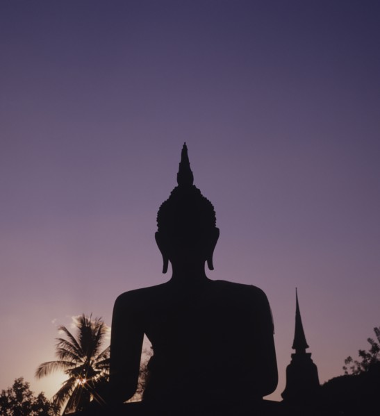 Thailand, Sukhothai, Wat Mahathat, Seated Buddha Statue silhouetted against purple coloured evening