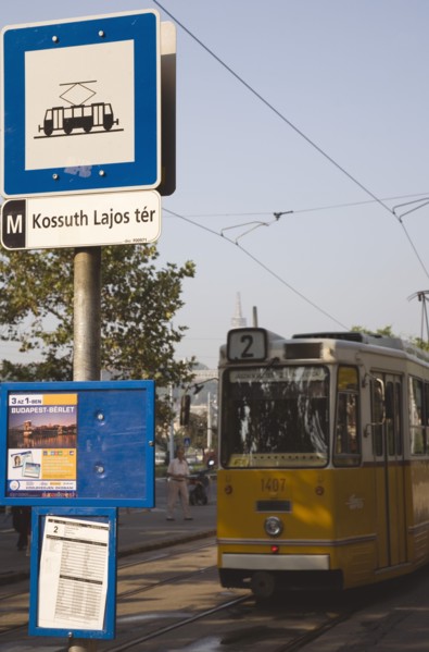 Budapest, Pest County, Hungary. Yellow tram approaching stop and signpost displaying timetable.