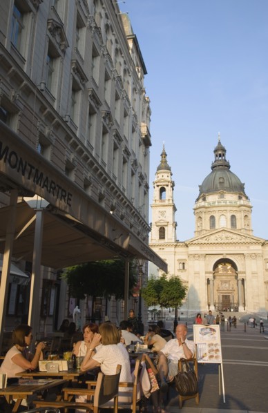 Budapest, Pest County, Hungary. Cafe with Summer tourists seated at outside tables with Saint