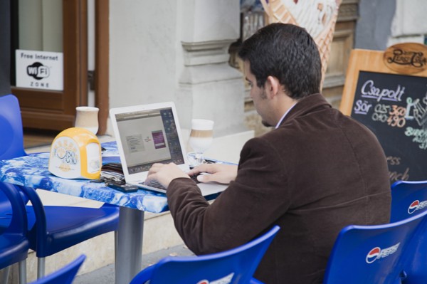 Budapest, Pest County, Hungary. Hungarian man has coffee at outside table while using laptop online