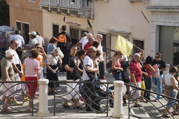 Venice, Veneto, Italy. Tour group of tourists crossing bridge in late summer led by guide holding